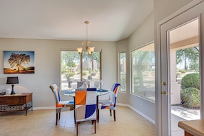 A dining area with a glass table, chairs with patterned upholstery, a chandelier, and a painting on the wall. - La Costa Chandler (Chandler)