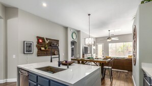 A modern kitchen with a large island, wooden flooring, and a dining area with a high ceiling fan. - Harrison Chandler (Chandler)