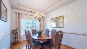 A dining room with a wooden table, six chairs, a chandelier, a mirror, and a window with blinds. - 530 Waterford Drive, Cartersville (Cartersville)