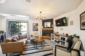 A modern living room with a sofa, ottoman, and coffee table, a fireplace, and a TV mounted on the wall. - 6380 Code & Comfort in Boston Commons (Englewood)