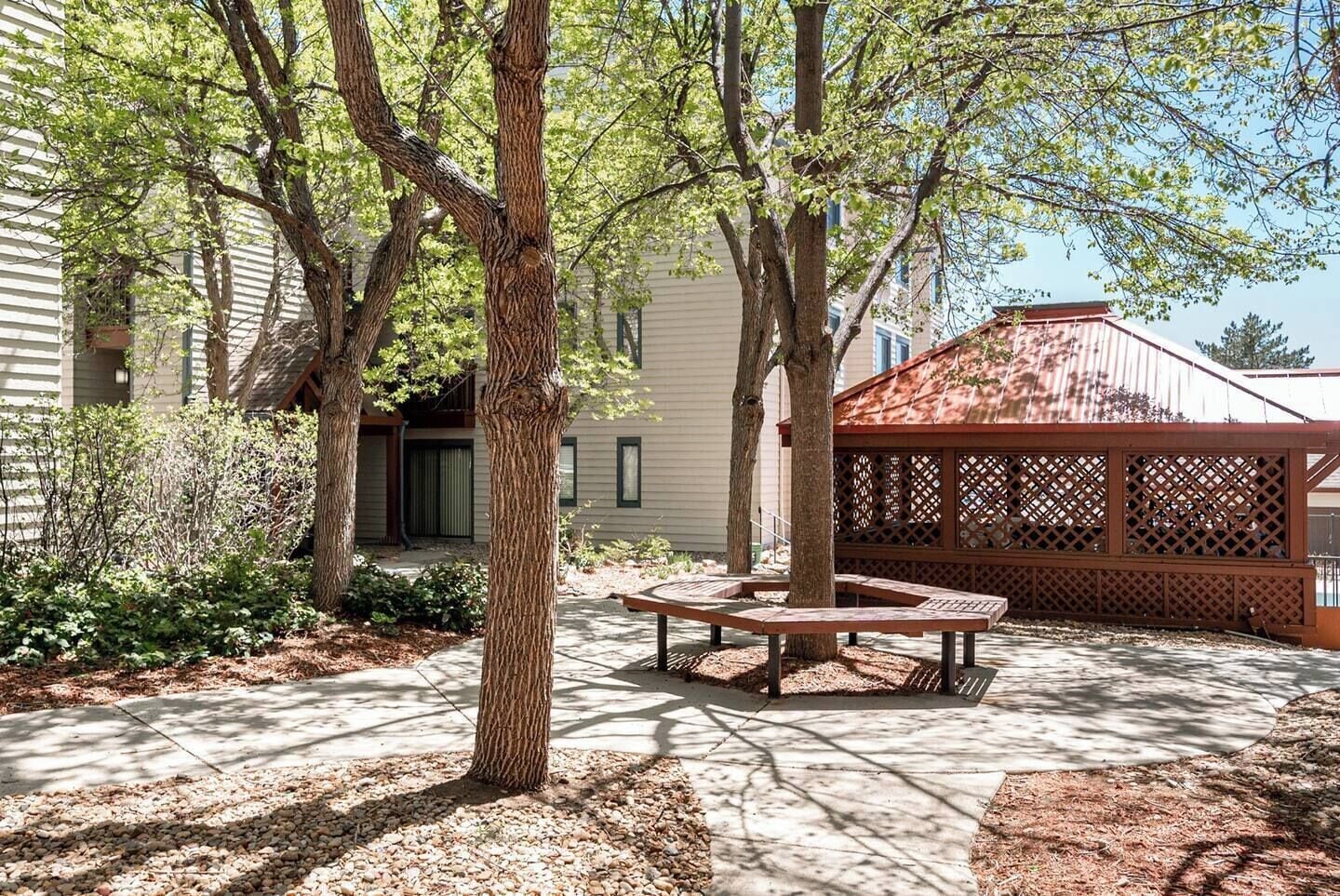 A courtyard with a wooden bench, trees, and a covered seating area.