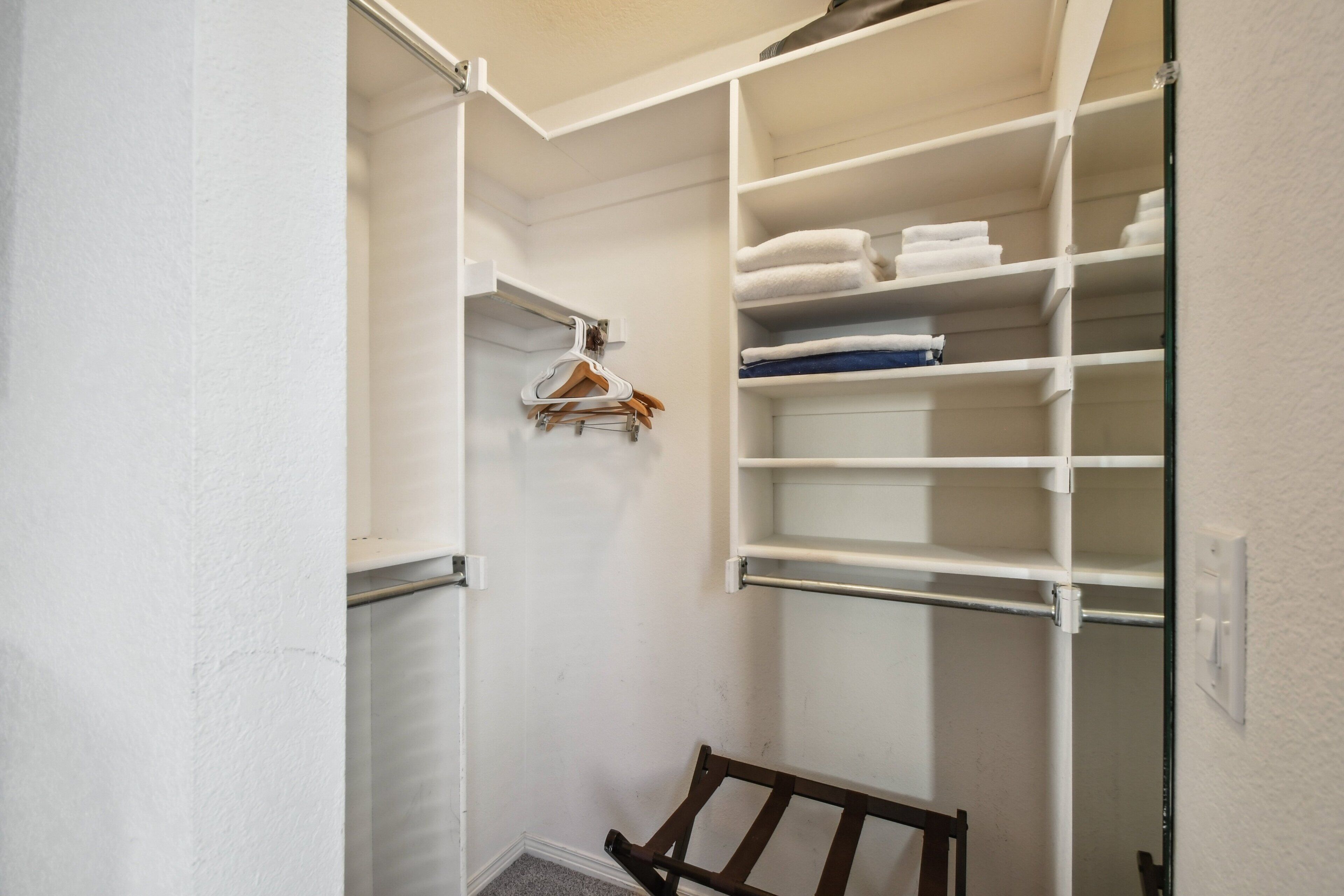 Een inloopkast met open planken, een houten bankje en hangende kleding.