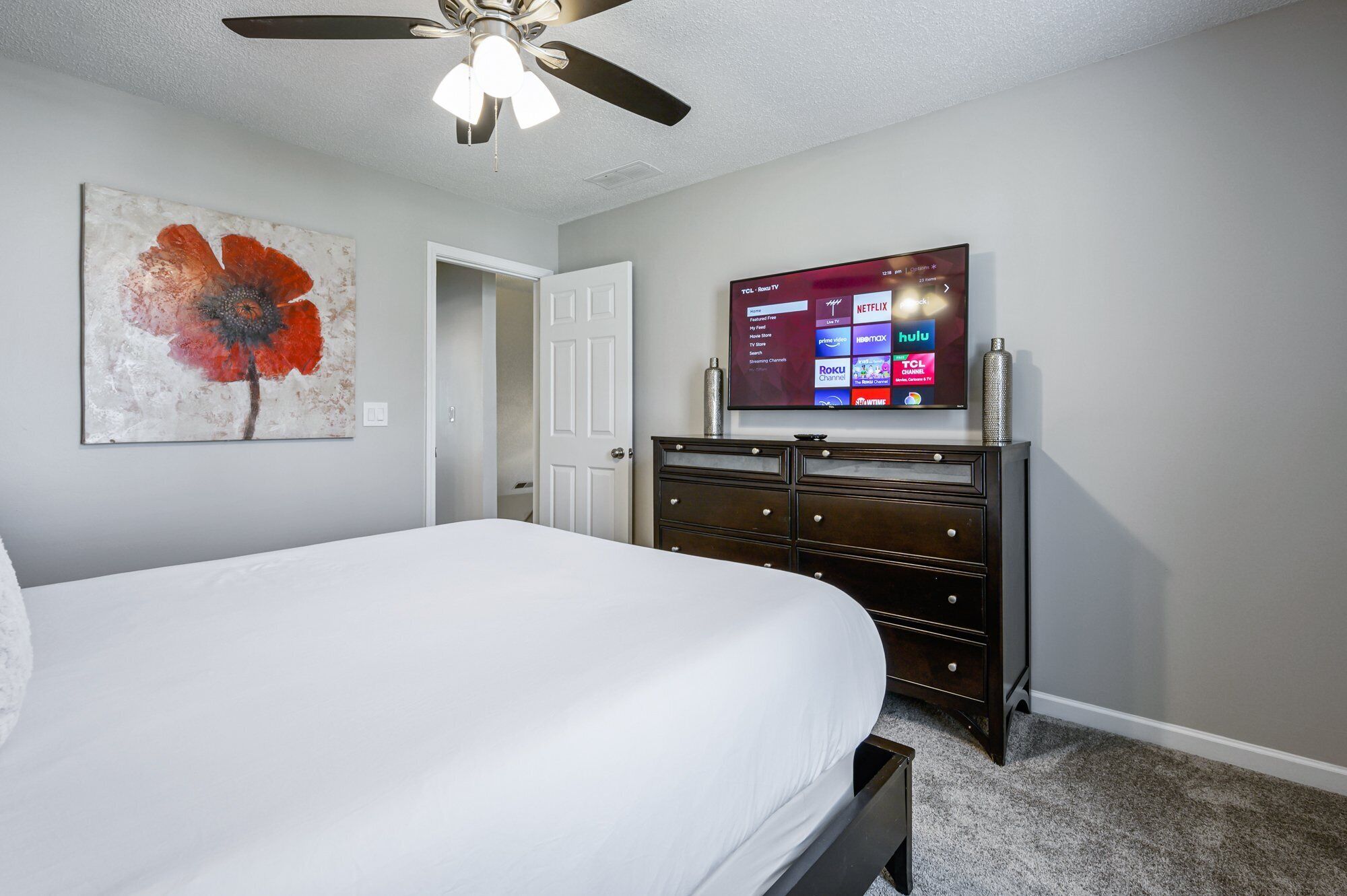 A bedroom with a bed, a ceiling fan, a TV mounted on the wall, and a dresser.