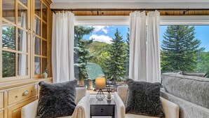 A cozy room with two beige sofas, a wooden cabinet, and a large window offering a view of a green landscape and trees. - 4925 Pike Unit1 (Cascade)