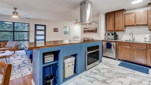 Una cocina moderna con una isla azul, electrodomésticos de acero inoxidable, armarios de madera y un amplio ventanal.