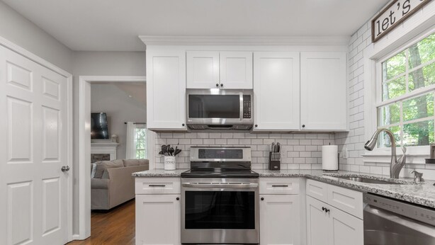 Una cocina moderna con armarios blancos, electrodomésticos de acero inoxidable y piso de madera.