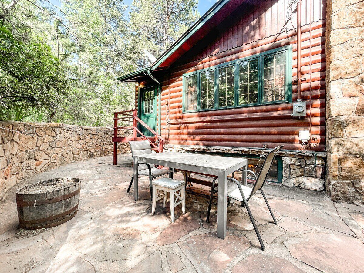 A rustic log cabin with a stone wall and a wooden table with chairs outside.