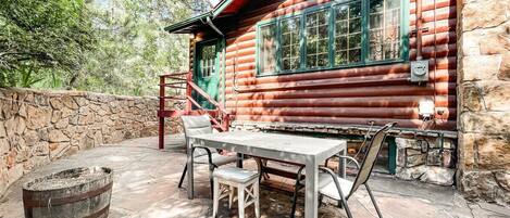 A rustic log cabin with a stone wall and a wooden table with chairs outside.