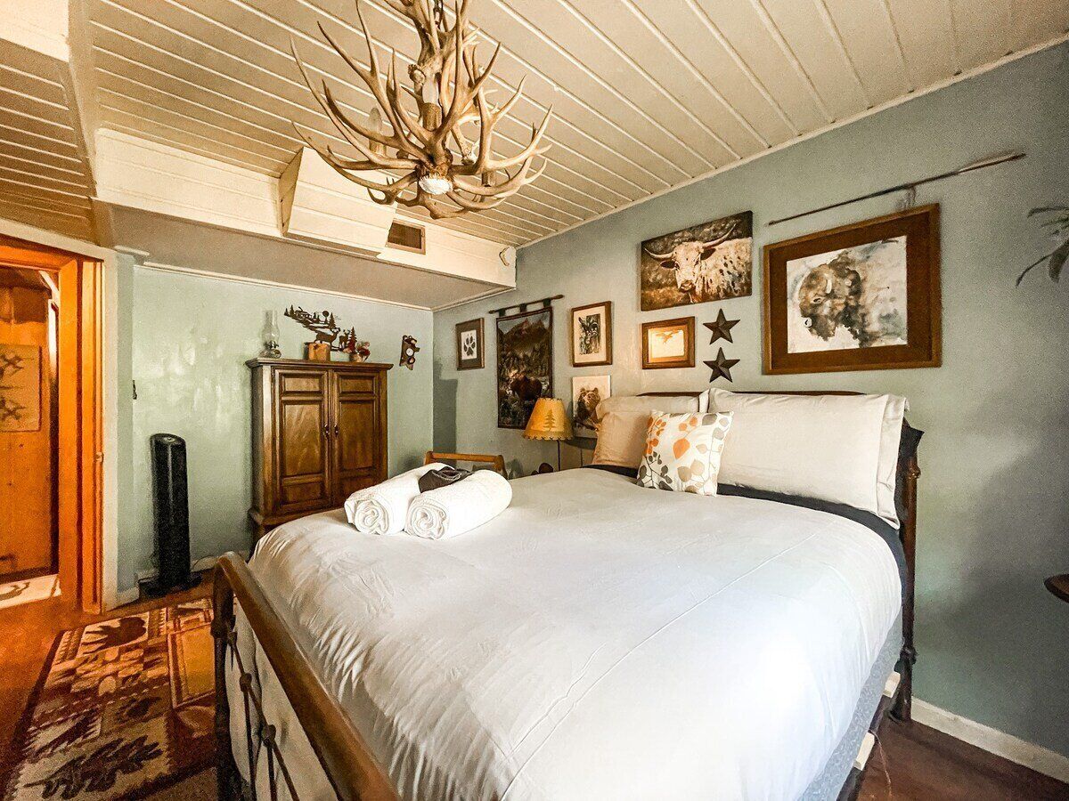 A bedroom with a large bed, a wooden headboard, a chandelier, and wall art.