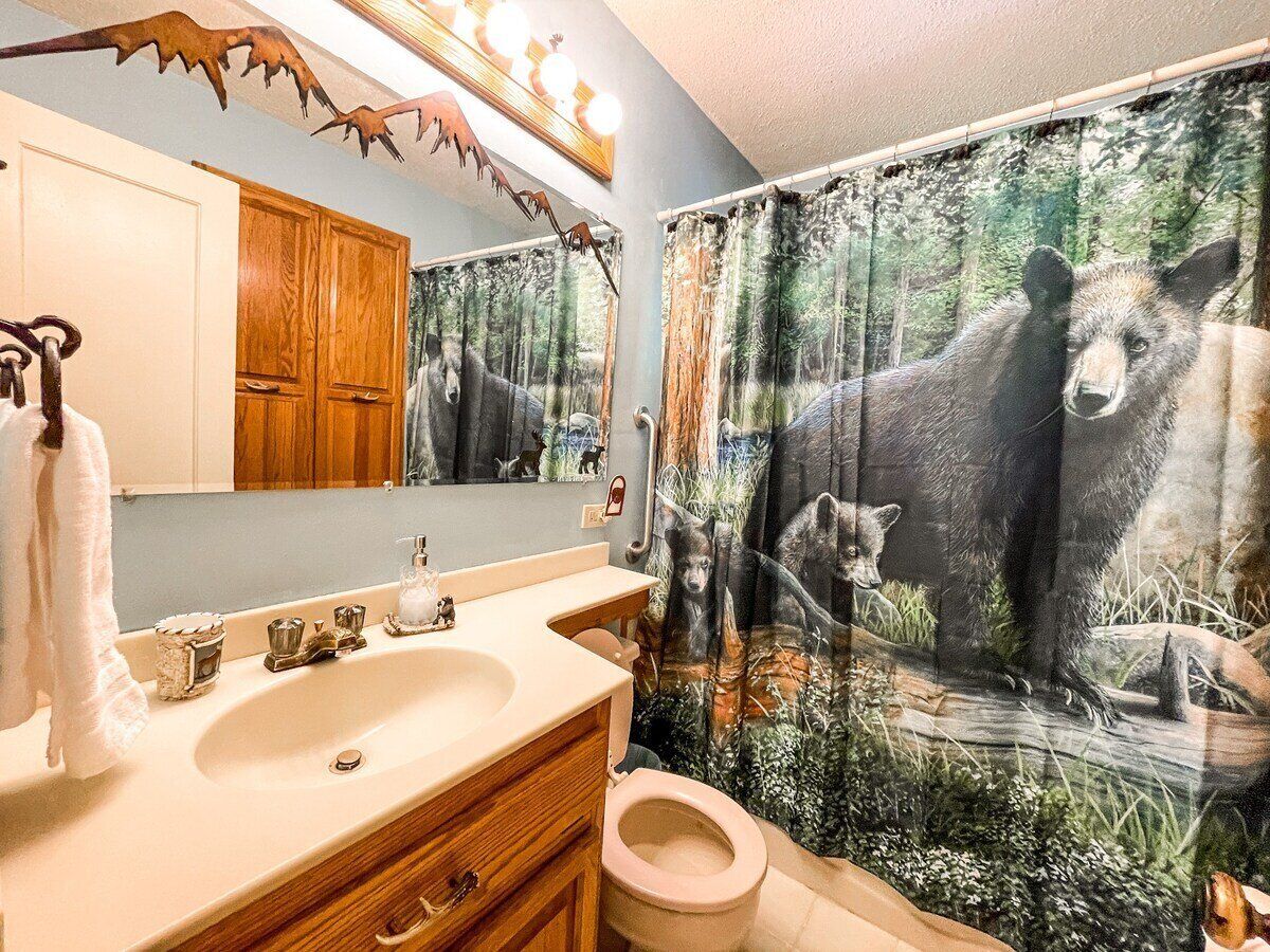 A bathroom with a wooden vanity, a sink, a mirror, a toilet, and a shower curtain with a bear design.