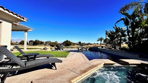 Ein Poolbereich mit Liegestühlen, einer Pergola und Blick auf einen Golfplatz.