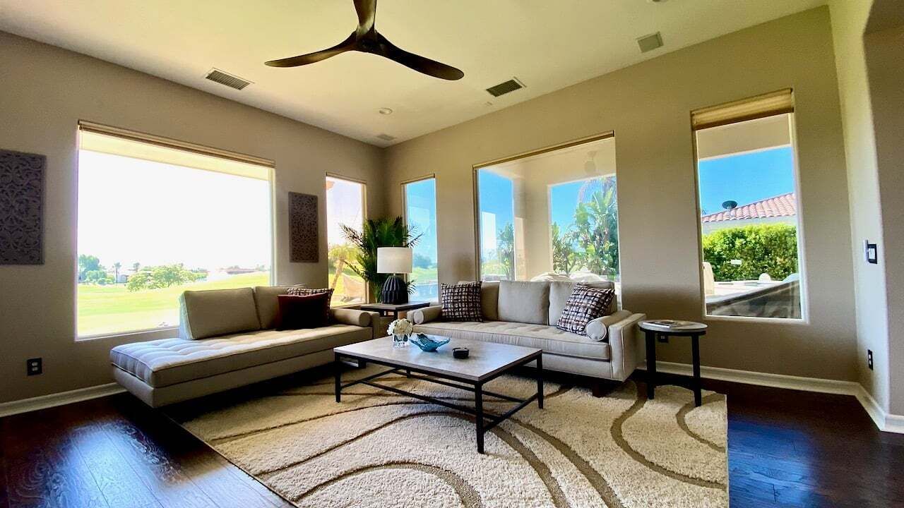 A spacious living room with a large window, a ceiling fan, and a sofa set.