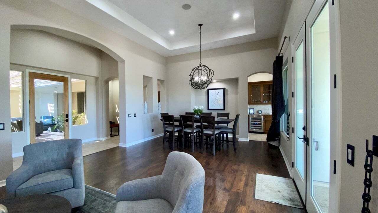A spacious living room with a dining area, hardwood floors, and a modern chandelier.