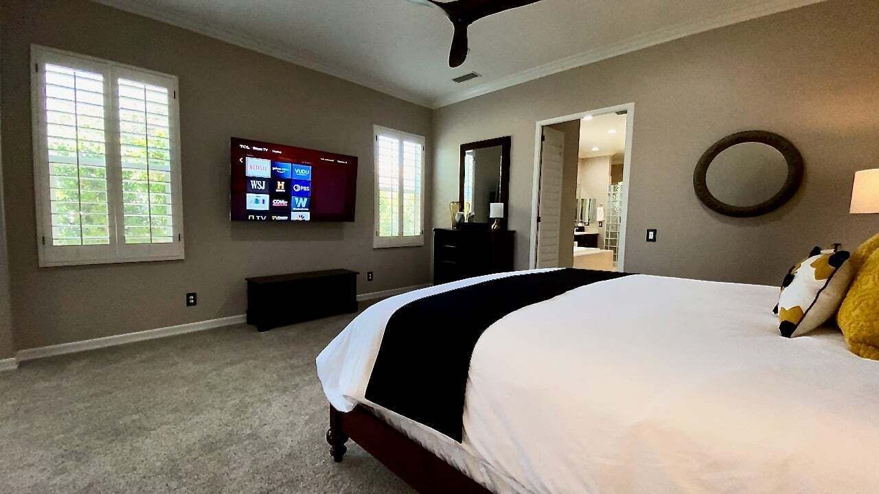 A bedroom with a large bed, a TV mounted on the wall, a dresser, and a mirror.