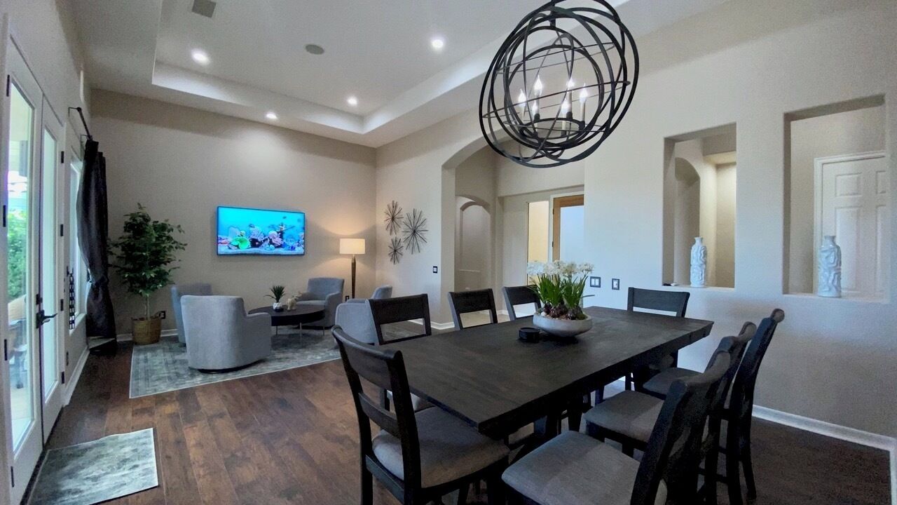 Un comedor amplio con una gran mesa de madera y sillas modernas, un televisor montado en la pared y una lámpara decorativa en el techo.