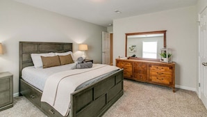 Une chambre à coucher avec un lit, des tables de chevet, une commode, un miroir et une porte.