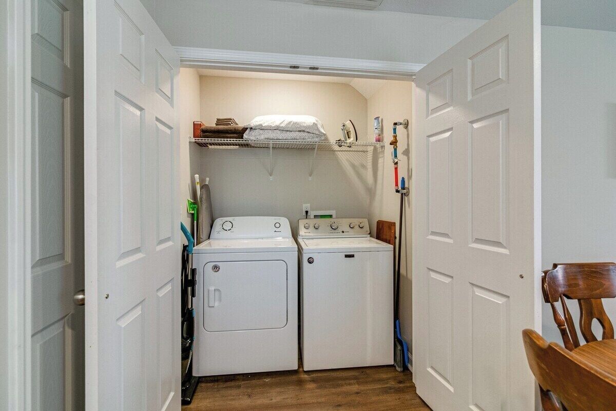 A laundry room with two stacked washers and dryers, a shelf with a towel, and a wooden chair.