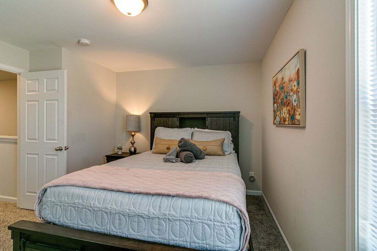 Une chambre à coucher avec un lit, une table de chevet, une lampe, une porte et un tableau au mur.