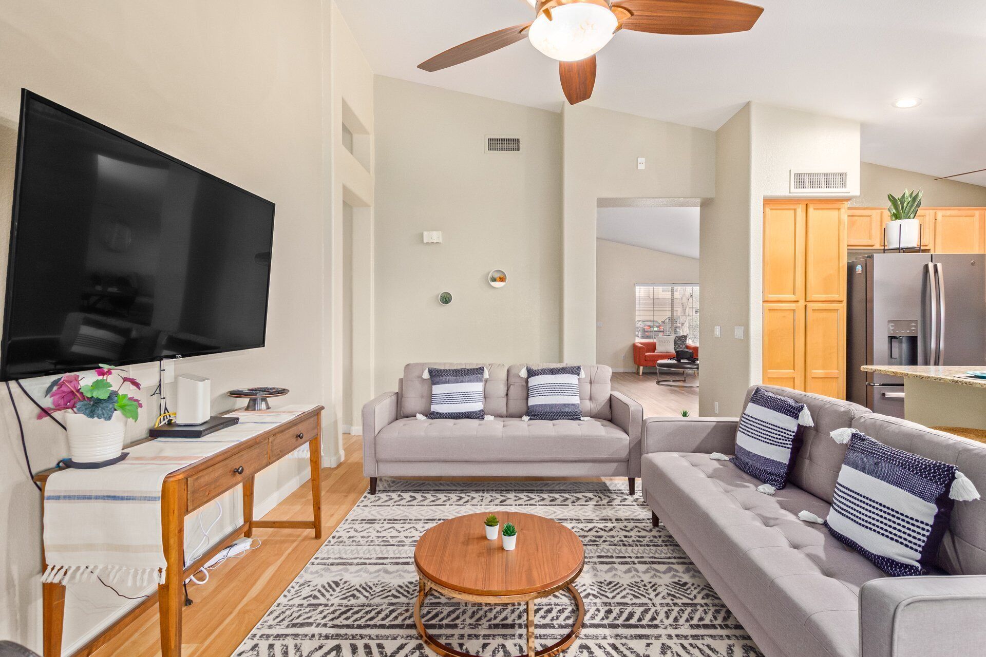 A modern living room with a flat-screen TV, grey sofas, a wooden coffee table, and a patterned rug.
