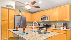 Una cocina con encimeras de granito, armarios de madera y electrodomésticos de acero inoxidable, además de un ventilador de techo.