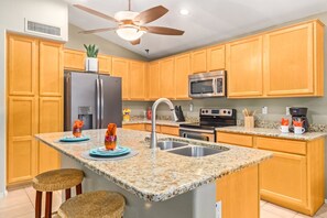 A kitchen with granite countertops, wooden cabinets, stainless steel appliances, and a ceiling fan. - Augusta Chandler (Chandler)