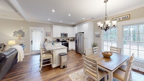 Una cocina moderna con muebles blancos, un refrigerador de acero inoxidable y un comedor con mesa y sillas de madera.