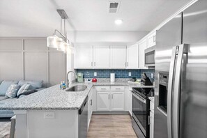 Una cocina moderna con armarios blancos, encimera de granito, electrodomésticos de acero inoxidable y salpicadero azul.