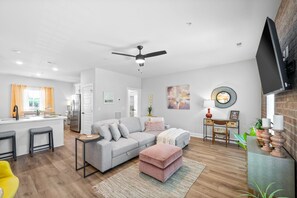 A modern living room with a grey sofa, a pink ottoman, and a dining area with a table and chairs. - The Spot 281 Liberty Pkwy (Clarksville)