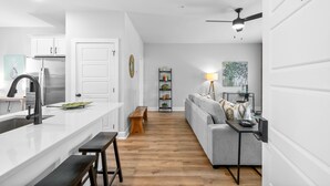 A modern kitchen with white cabinetry, a central island with a sink, and a dining area with a bench. - The Spot 281 Liberty Pkwy (Clarksville)