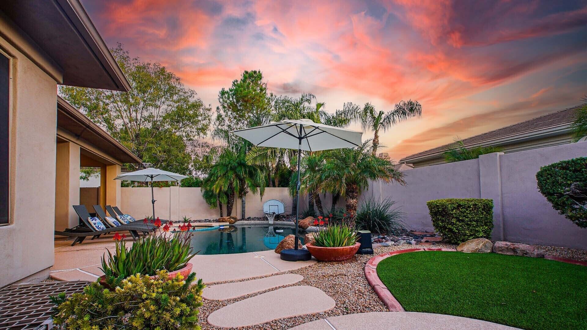 A backyard with a swimming pool, lounge chairs, and a basketball hoop.