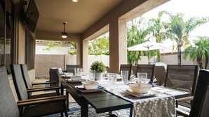 Un área de comedor al aire libre con una mesa larga dispuesta para seis personas, rodeada de sillas de mimbre.