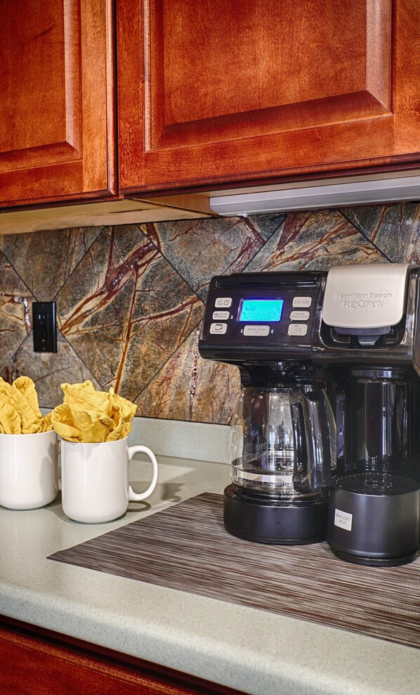 A coffee maker with a digital display, two white mugs, and a cloth bag on a kitchen counter. - Lynx Chandler/ocotillo (Chandler)