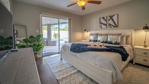 A bedroom with a bed, ceiling fan, bedside tables, and a view of the outdoors. - Central Chandler (Chandler)