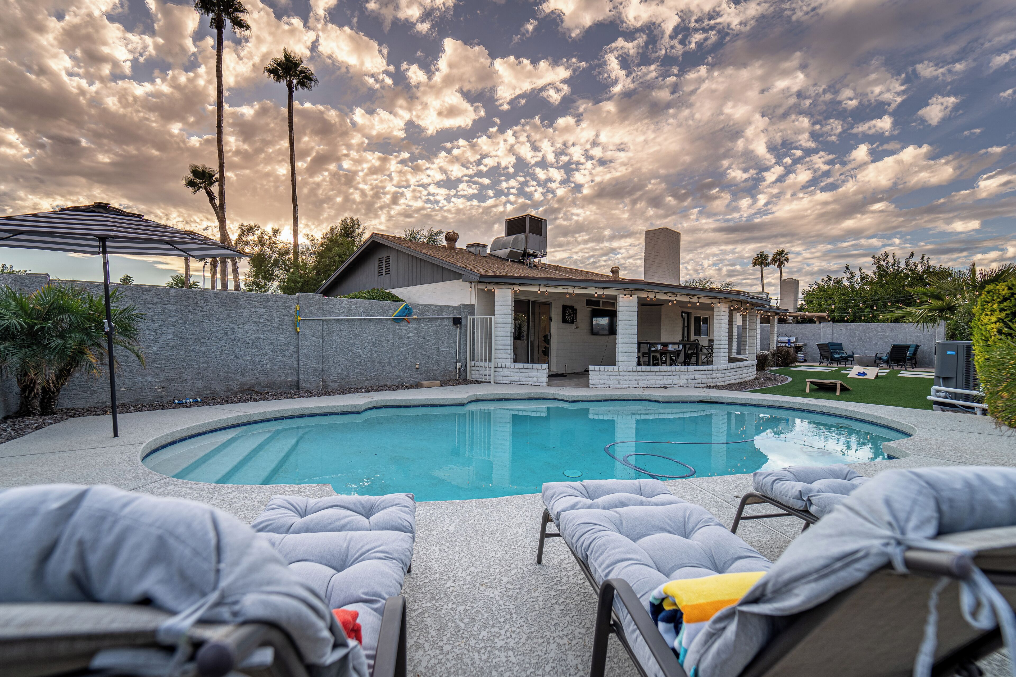 A backyard with a swimming pool, lounge chairs, and a patio area.