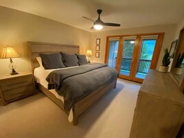Un dormitorio con cama, mesitas de noche, ventilador de techo y puerta corrediza al exterior.