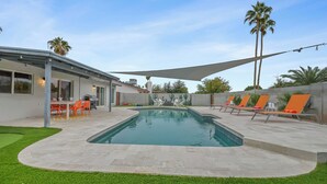 A modern outdoor pool area with a patio, lounge chairs, and a dining setup. - Loughlin Chandler (Chandler)