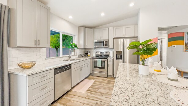 A modern kitchen with white cabinets, stainless steel appliances, and a large window with a view of greenery. - Loughlin Chandler (Chandler)