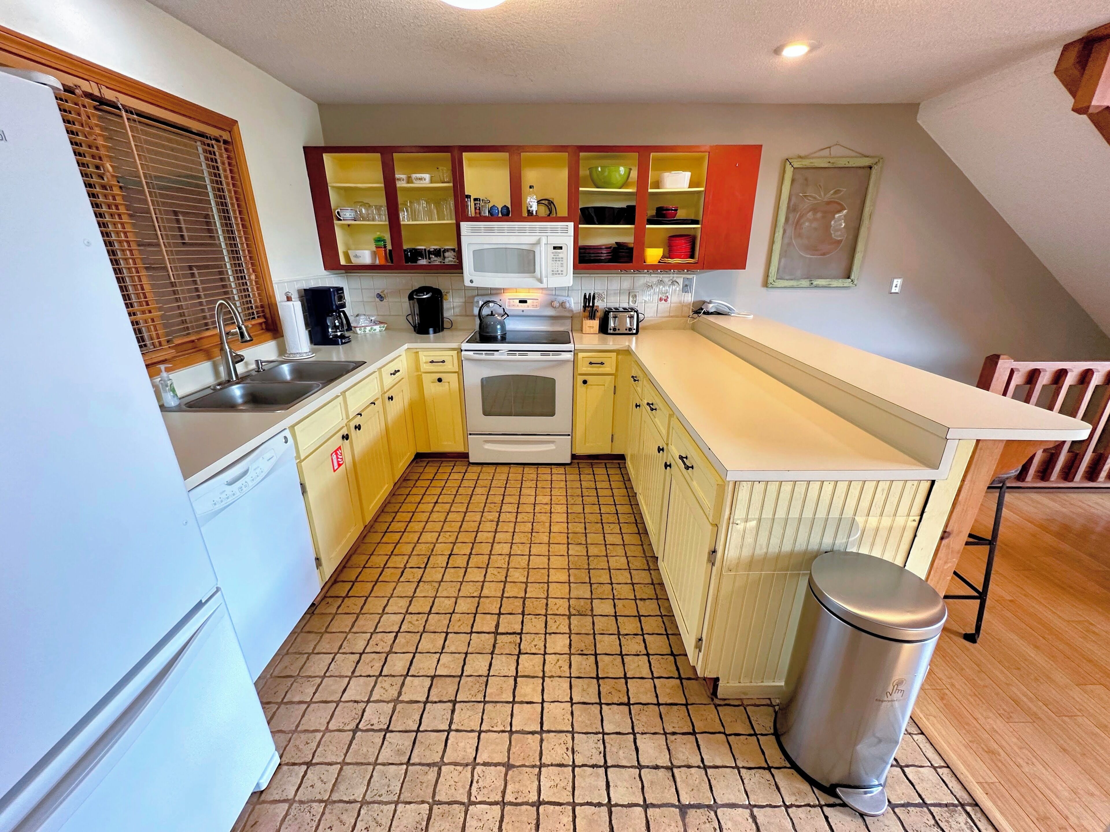 Una cocina compacta con piso de baldosas, microondas integrado, estufa y pileta.