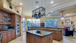 A spacious kitchen with wooden cabinets, a large island, and hanging pots. - Tonto Chandler (Chandler)