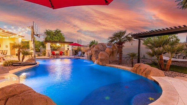 A swimming pool with a waterfall feature, surrounded by rocks and palm trees. - Tonto Chandler (Chandler)
