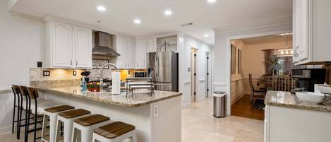 A modern kitchen with white cabinetry, a central island with stools, stainless steel appliances, and recessed ceiling lighting.