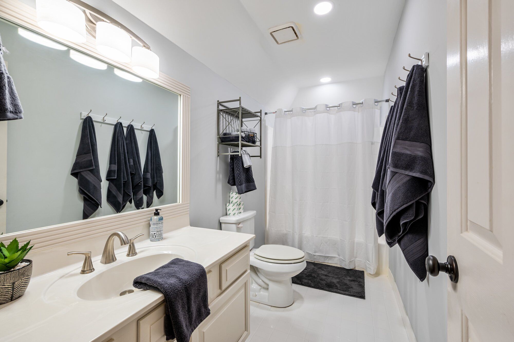 A modern bathroom with a white sink, two faucets, a mirror, a toilet, and a shower curtain.