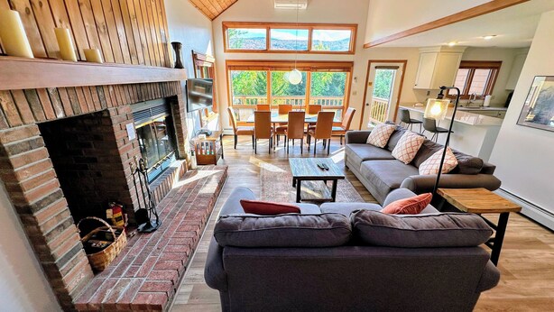A spacious living room with a fireplace, a sofa, a dining area, and large windows offering a view of the outdoors. - Mwp29 (Bretton Woods)
