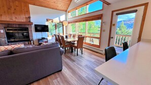 A spacious living area with a fireplace, a TV, a dining table with chairs, and large windows offering a view of the outdoors. - Mwp29 (Bretton Woods)