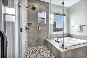 Une salle de bain moderne dotée d’une douche à parois de verre, d’une grande baignoire et d’une fenêtre laissant entrer la lumière naturelle.