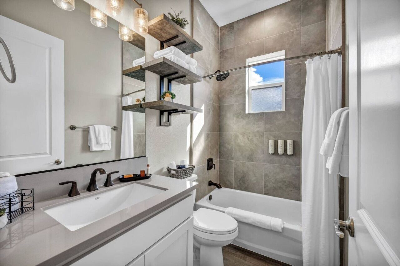 A modern bathroom with a large sink, toilet, and bathtub. There are shelves above the sink and a window above the bathtub.