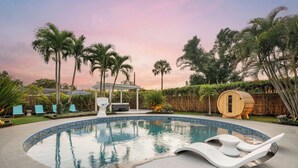 Ein kreisförmiger Swimmingpool mit Liegestühlen und einer Holzsauna.