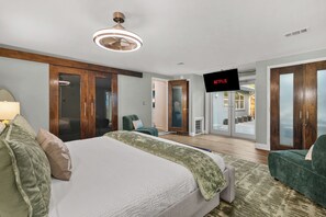 Et moderne hotelværelse med en stor seng, et fjernsyn og en skydedør, der fører til en balkon.