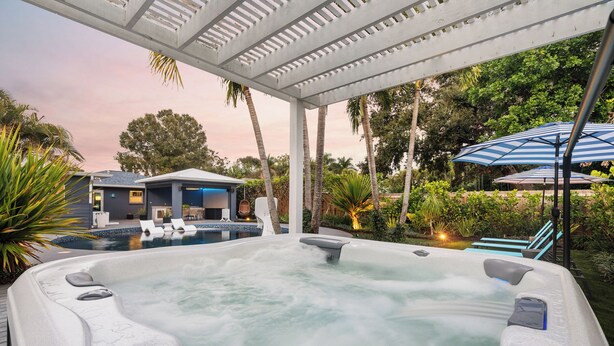 Ein Whirlpool mit einer Holzterrasse und Liegestühlen, umgeben von üppiger Vegetation und einem Pool.