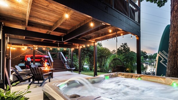 A hot tub with water jets, a covered seating area with chairs, and a view of a body of water. - Lakefront + Kayaks + Dock + Screened in Porch | Home Sweet Bowen (Inman)